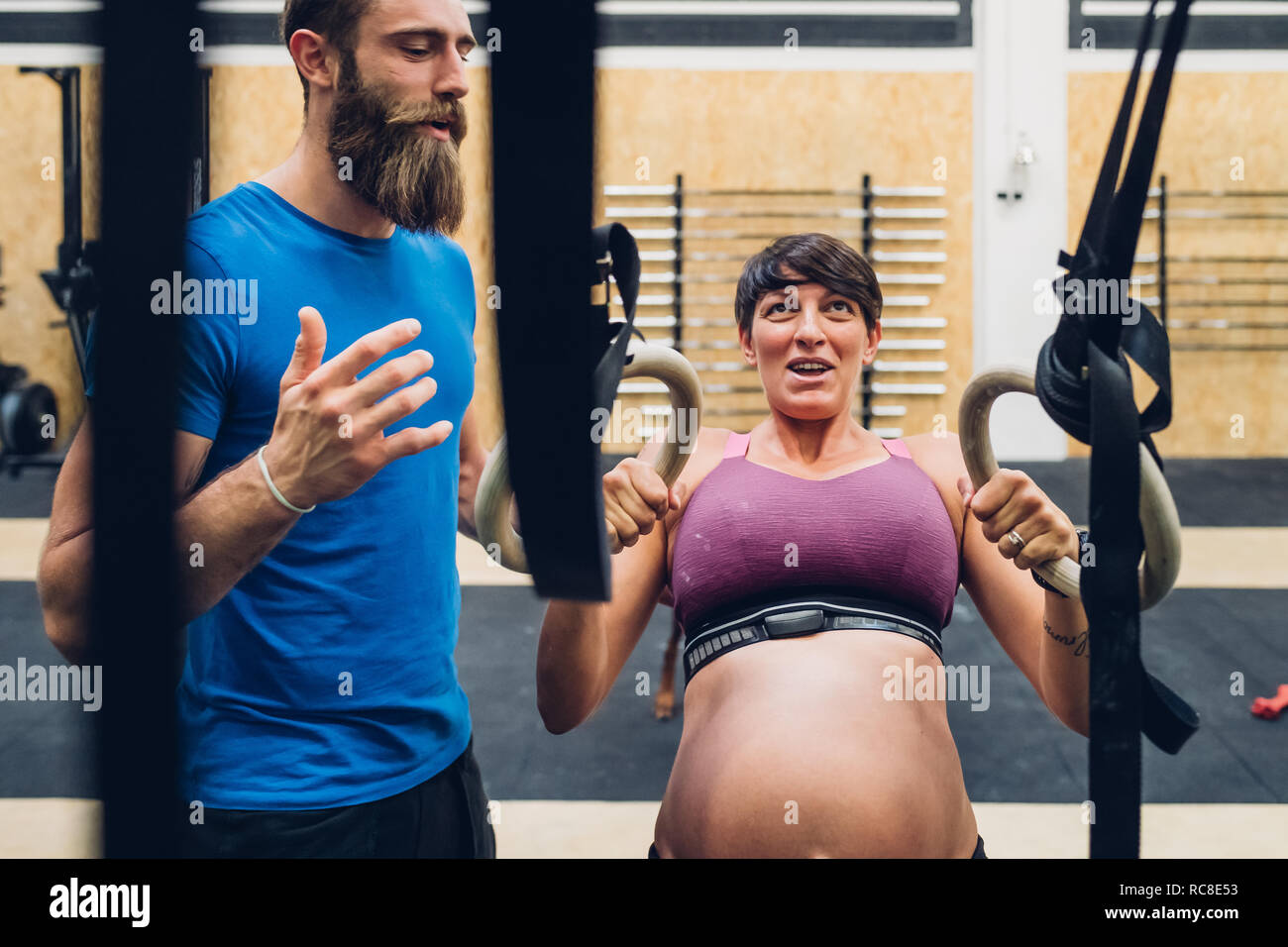 Trainer führen schwangere Frau mit Trainingsgeräten in der Turnhalle Stockfoto