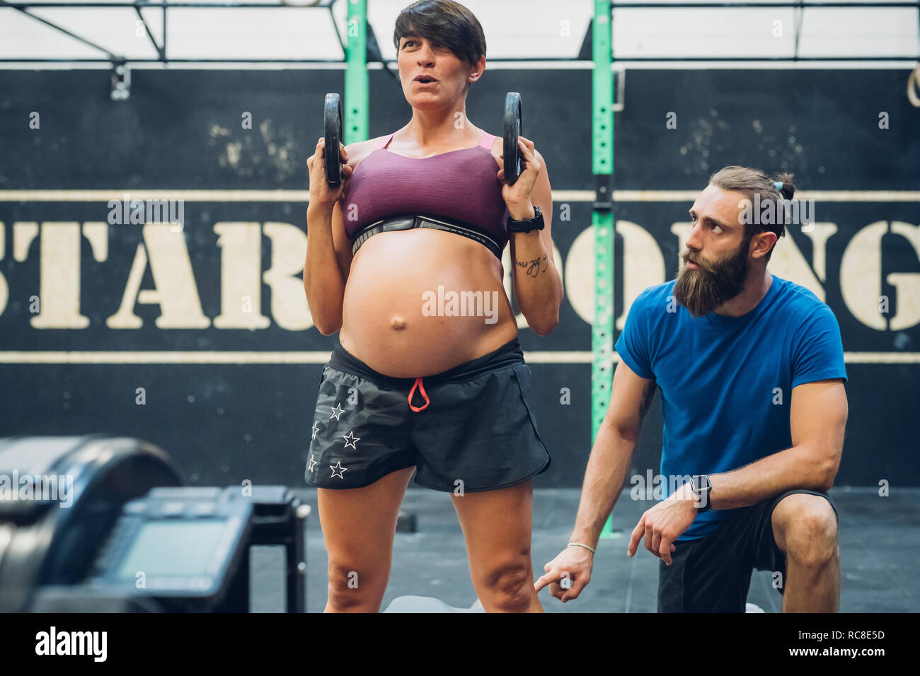 Trainer führen schwangere Frau mit Gewichten in der Turnhalle Stockfoto