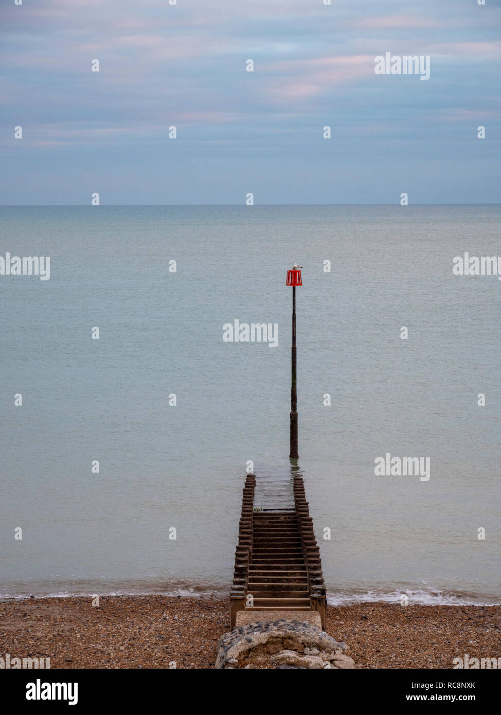 Einen Blick auf die roten Marker post und buhnen am Strand sshingle in Eastbourne Großbritannien an einem bewölkten Wintertag mit gedeckten Farben. Stockfoto