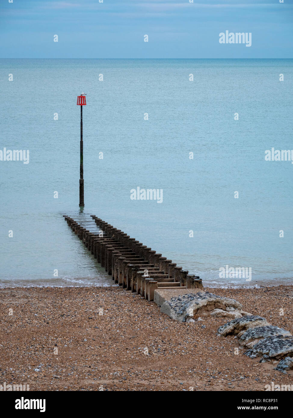 Einen Blick auf die roten Marker post und buhnen am Strand sshingle in Eastbourne Großbritannien an einem bewölkten Wintertag mit gedeckten Farben. Stockfoto