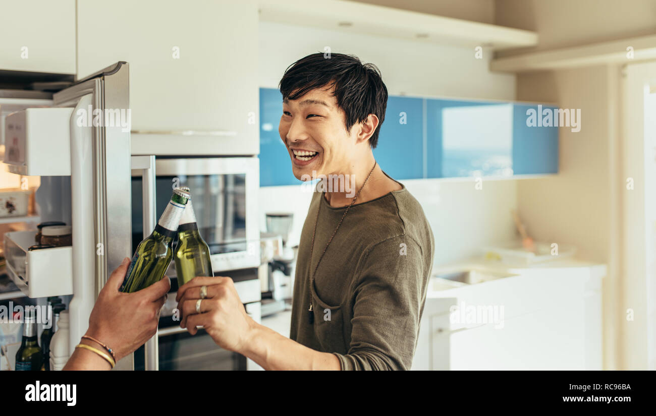 Lächelnd asiatischer Mann zu Hause stehend Toasten eine Flasche Bier mit seinem Freund. Freunde eine Party zu Hause mit Bierflaschen. Stockfoto