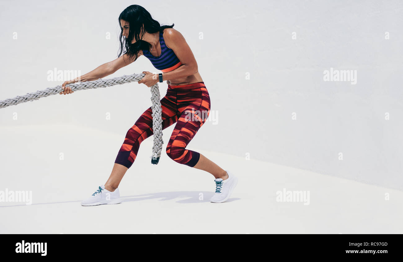 Frau in Fitness verschleiß Ziehen einer Schlacht Seil. Athletische Frau tun Krafttraining durch Ziehen einer Schlacht Seil. Stockfoto