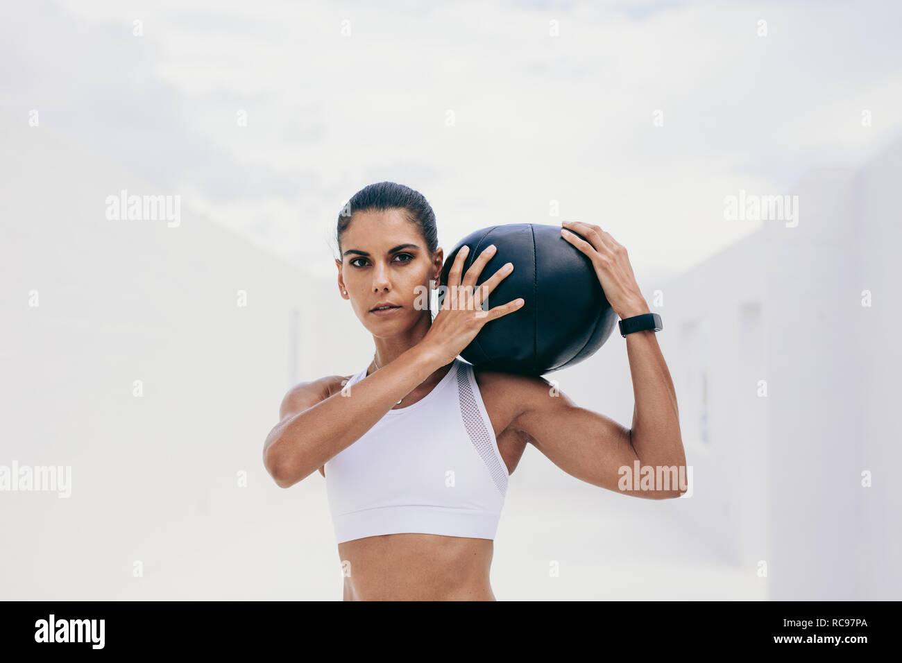 Fitnesstraining-Frau, die einen Medizinball auf der Schulter hält. Sportlerin trainiert mit einem Medizinball. Stockfoto