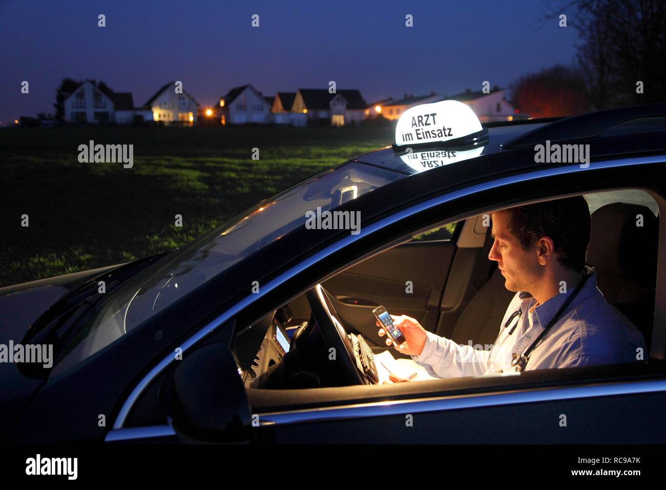 Junge GP, Arzt für Allgemeinmedizin im Land arbeiten, die anrufen und sich Notizen in seinem Auto nach einem Abend home Stockfoto