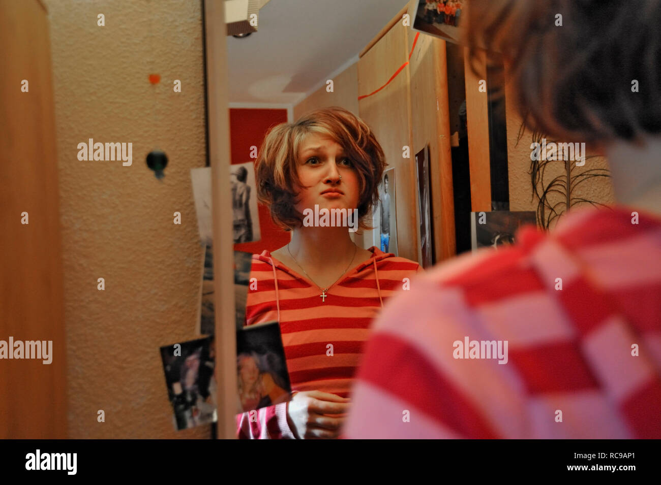 Junge Frau zieht Grimassen vor dem Spiegel in ihrem Zimmer | junge Frau, die lustige Grimassen vor dem Spiegel in ihrem Zimmer Stockfoto