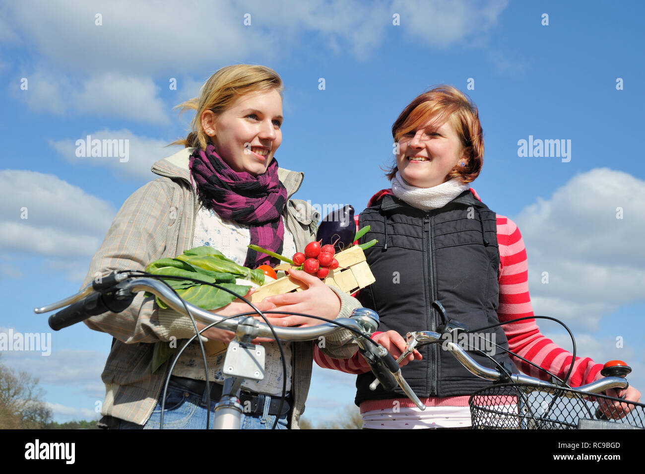 Zwei jungendliche Frauen mit Fahrrad und Gemüsekorb - junges Gemüse | zwei junge Frauen mit ihrem Fahrrad und ein Gemüse Warenkorb Stockfoto