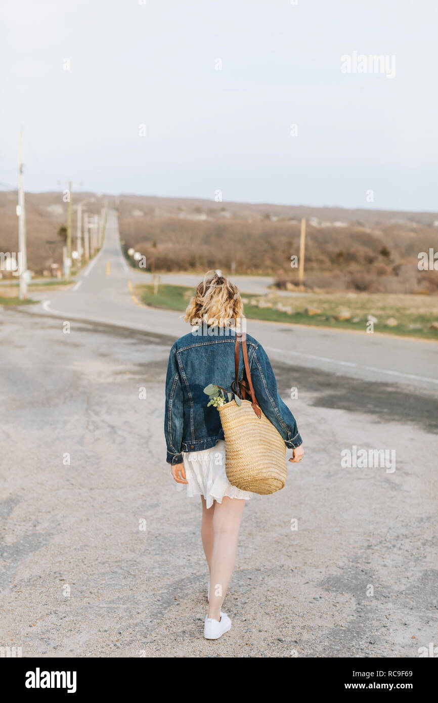 Junge Frau zu Fuß in Richtung Landstraße, Rückansicht, Menemsha, Martha's Vineyard, Massachusetts, USA Stockfoto