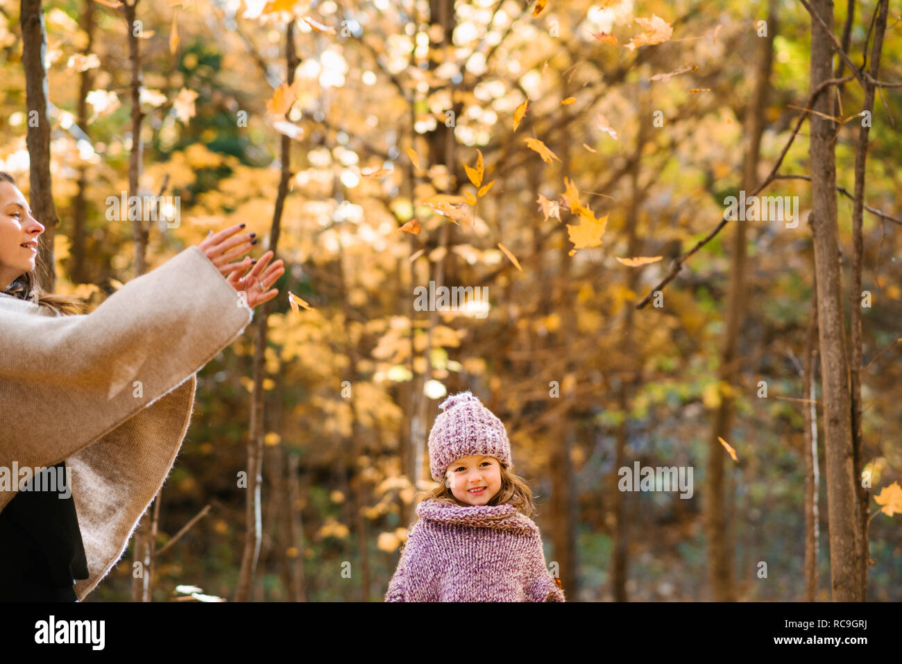 Mutter und Tochter werfen Blätter im Herbst in der Luft im Wald Stockfoto