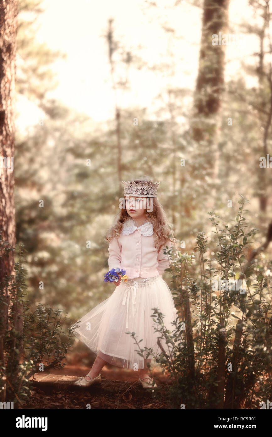 Kleines Mädchen alle gekleidet die stehen im Wald eine Krone trägt und mit Blumen in der Hand. Stockfoto