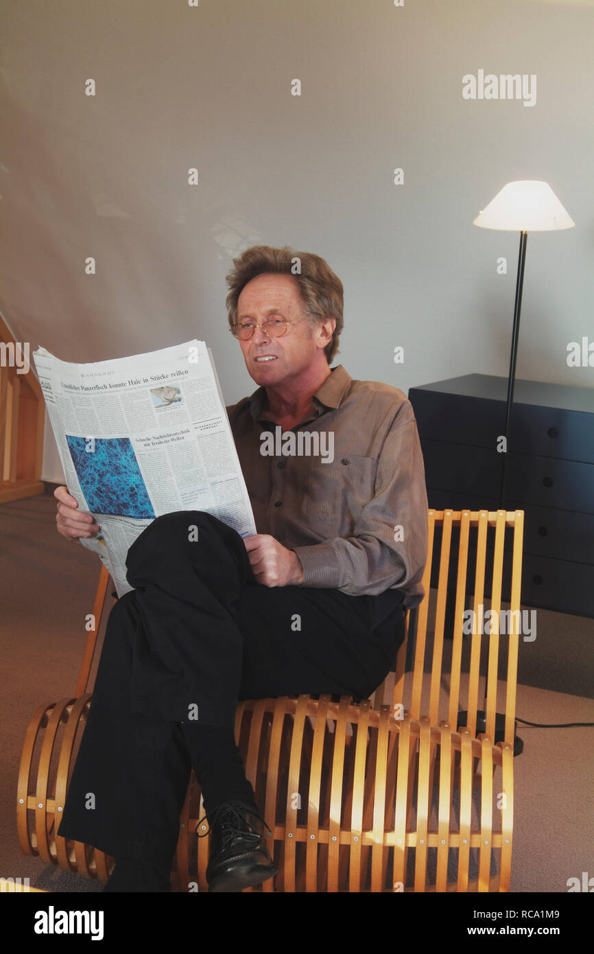 Mann mittleren Ändert liegst Zeitung in einem Stuhl | Mann mittleren Alters ist eine Zeitung lesen auf einem Stuhl Stockfoto