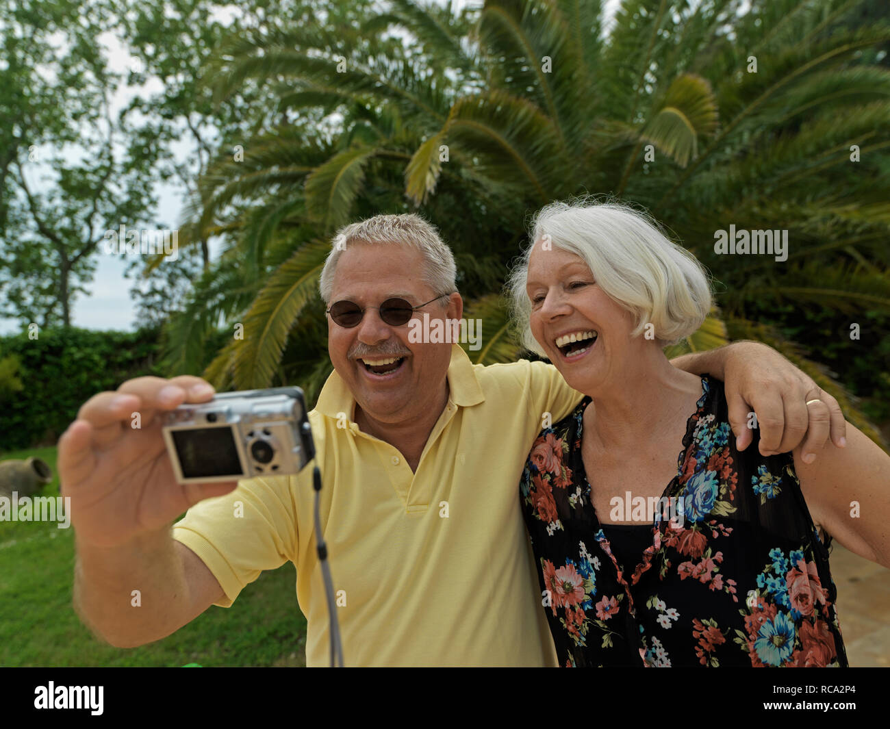 Älteres Ehepaar vor Palme fotografiert sich selbst | ältere Paare vor einer Palme, ein Bild von sich selbst Stockfoto