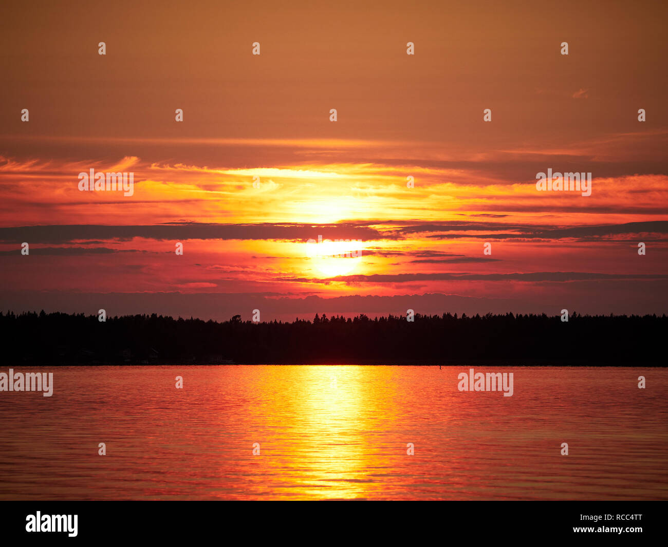 Roter Sonnenuntergang Himmel mit der Sonne und bunten Wolken über einem ruhigen Meer in Vaasa, Finnland. Die helle Scheibe der Sonne wird teilweise von Wolken verdeckt. Stockfoto
