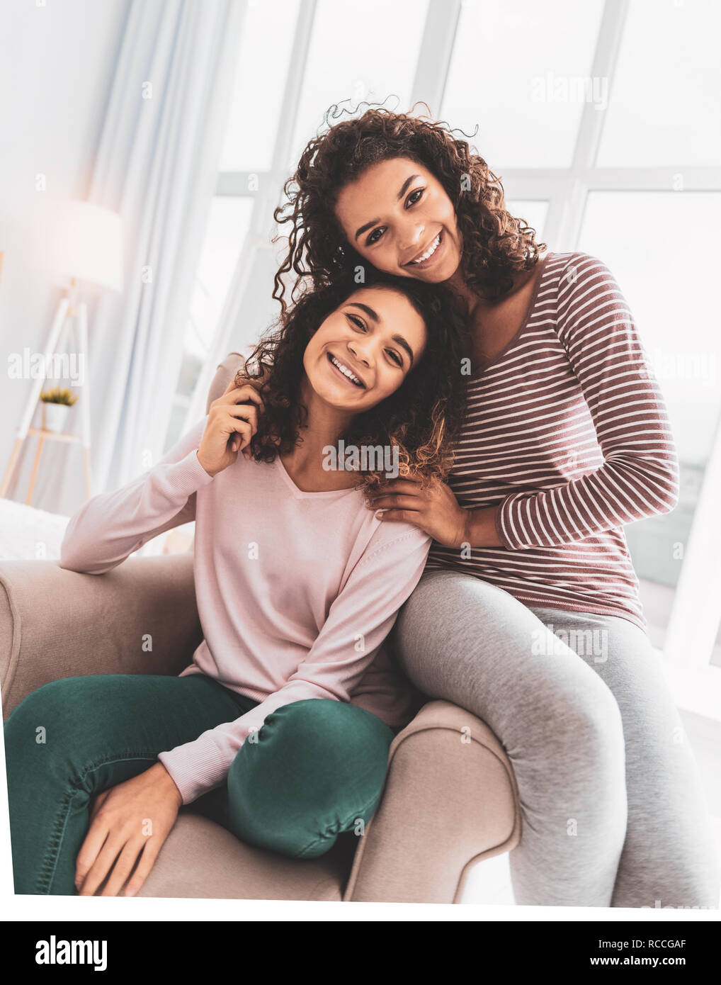 Lächelnde Schwester in Grau Leggings in der Nähe von ihrer älteren Schwester sitzen Stockfoto