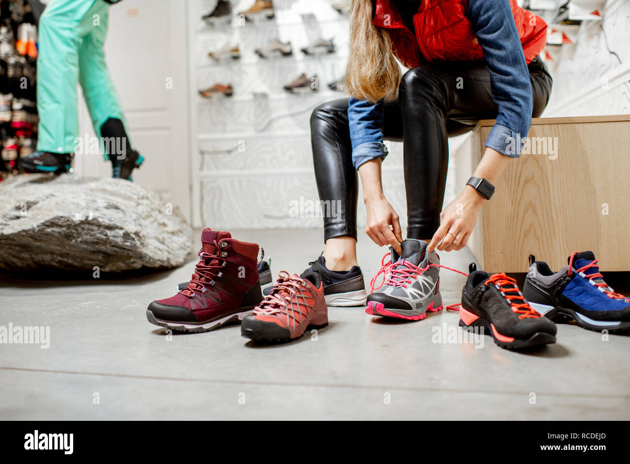 Frau, die versucht, verschiedene trail Schuhe für Wandern im Sportgeschäft, Nahaufnahme mit kein Gesicht Stockfoto