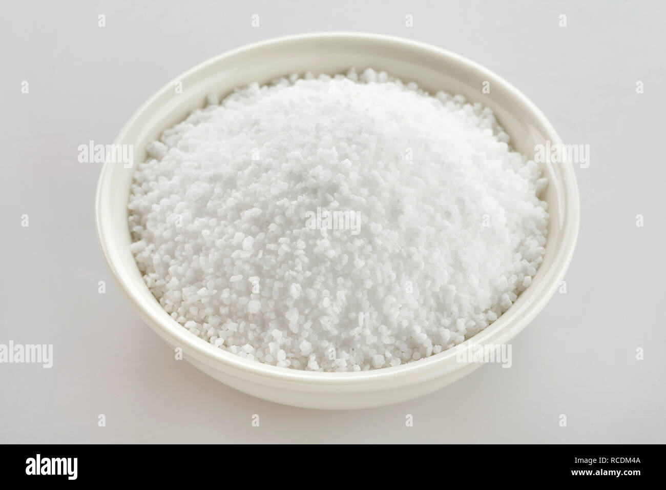 Schüssel aus weißem Fleur de Sel Salz durch Verdunstung an der Oberfläche des Meerwassers über einem weißen Hintergrund Stockfoto