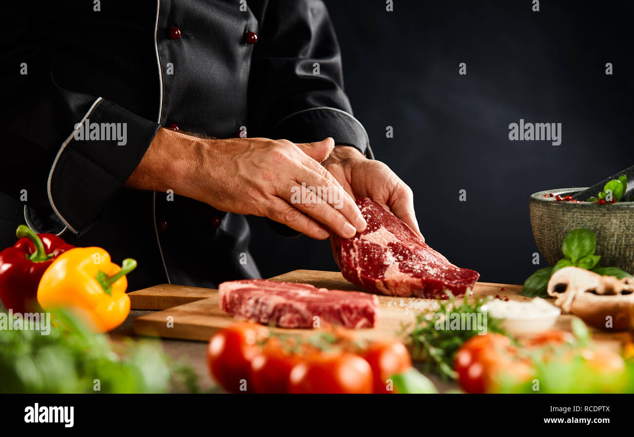 Koch Würze eines dicken rohes Rindfleisch Steak mit Spice Rub auf einem  Holzbrett mit frischem Gemüse und Kräutern in einer Nahaufnahme der Hand  Stockfotografie - Alamy