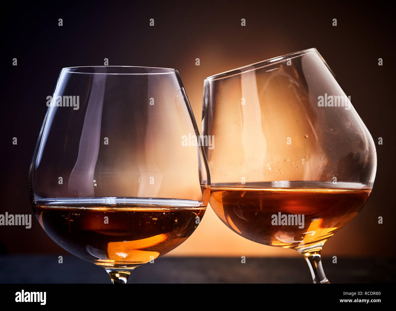 Zwei Gläser cognac Klirren in close-up gegen dunkelbraunen Hintergrund Stockfoto