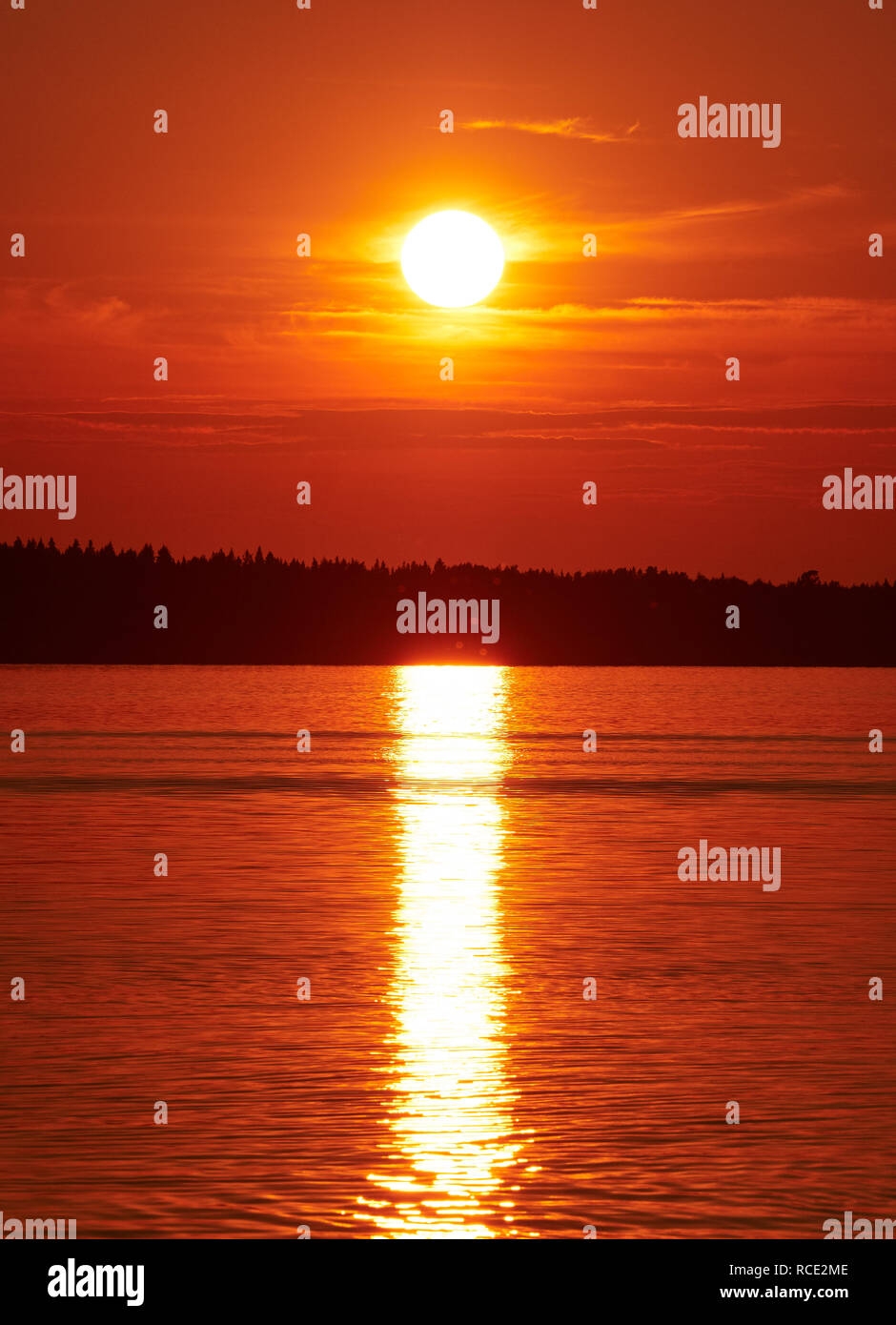 Roter Sonnenuntergang Himmel mit der Sonne und bunten Wolken über ruhige See Wasser in Vaasa, Finnland. Die helle Scheibe der Sonne wird teilweise von Wolken verdeckt. Ser Stockfoto