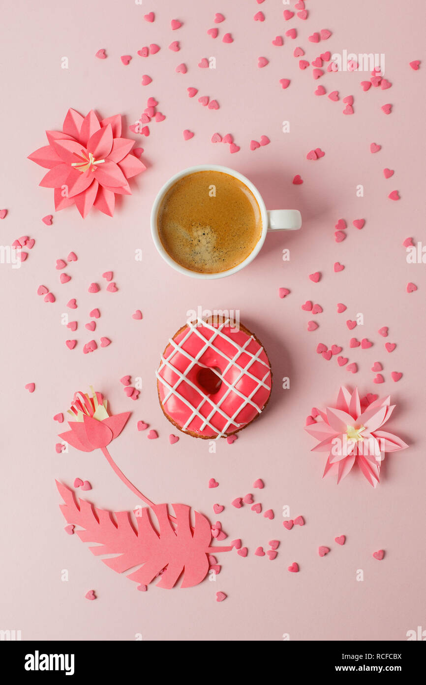 Iced Donut mit gestreiften Dekor und Tasse Espresso auf einem rosa Hintergrund in Pastelltönen mit modernen origami Papier Handwerk Dekor Blumen, Konzept der Frühstück Stockfoto