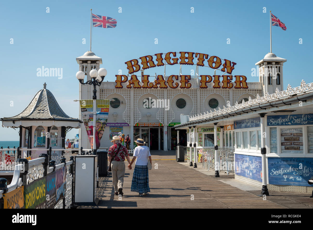 Ein paar walks​ Hand in Hand entlang Brighton Palace Pier an einem Sommertag. Stockfoto