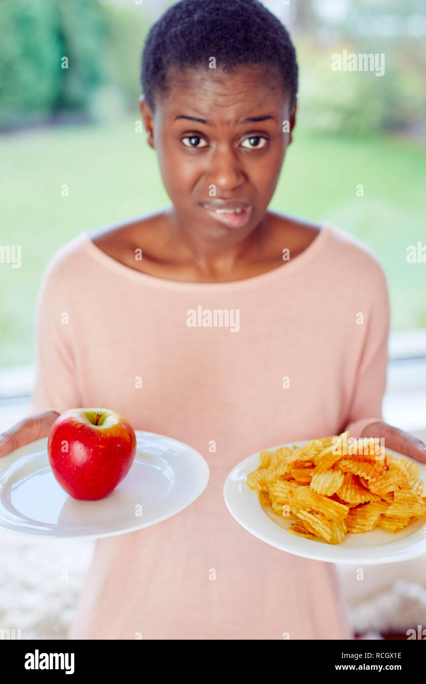 Ethnische Mädchen unentschlossen, ob Chips oder einen Apfel zu essen Stockfoto