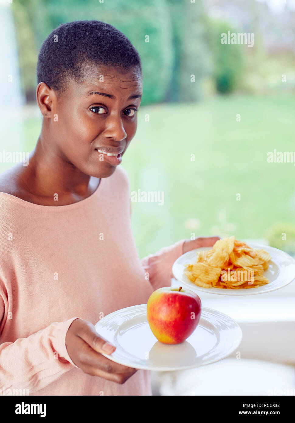 Ethnische Mädchen unentschlossen, ob Chips oder einen Apfel zu essen Stockfoto