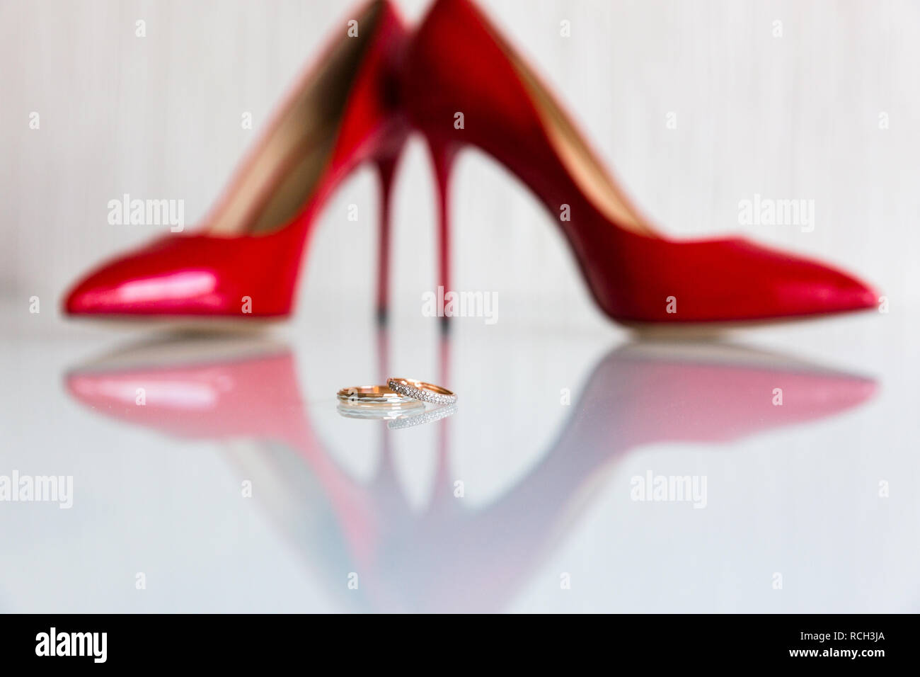 Ein paar Trauringe auf die spiegelfläche auf dem Hintergrund der roten Heels Stockfoto