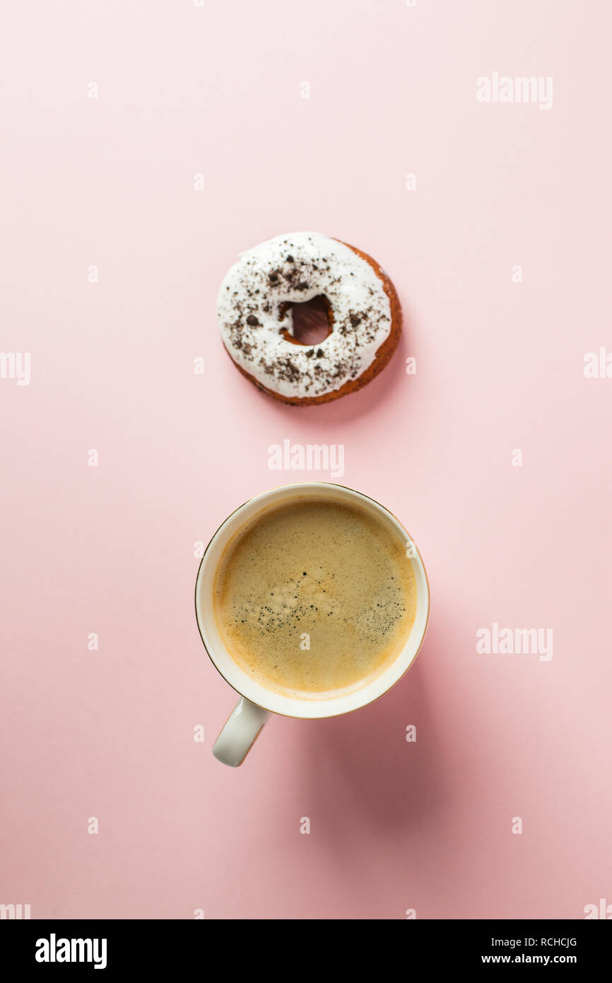 Iced Donut mit Schokolade Dekor und Tasse Espresso auf einem Rosa pastell Hintergrund, minimale Konzept der Frühstück Stockfoto