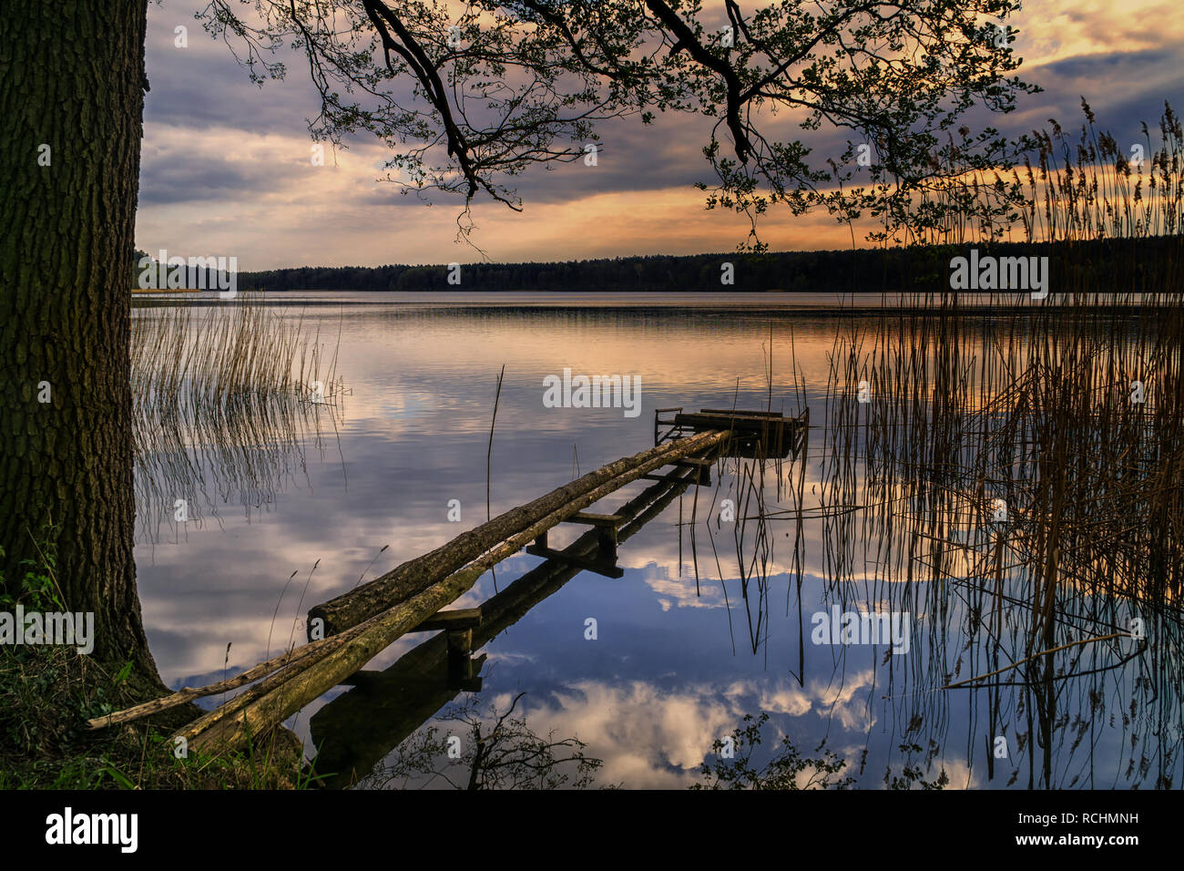 Ein malerischer Blick auf den See in der Abenddämmerung in Brodnica Seenplatte, Polen, Europa. Sonniger Frühlingstag. Eine Fußgängerbrücke mit einer Plattform, die von lokalen anglers gebaut. Stockfoto