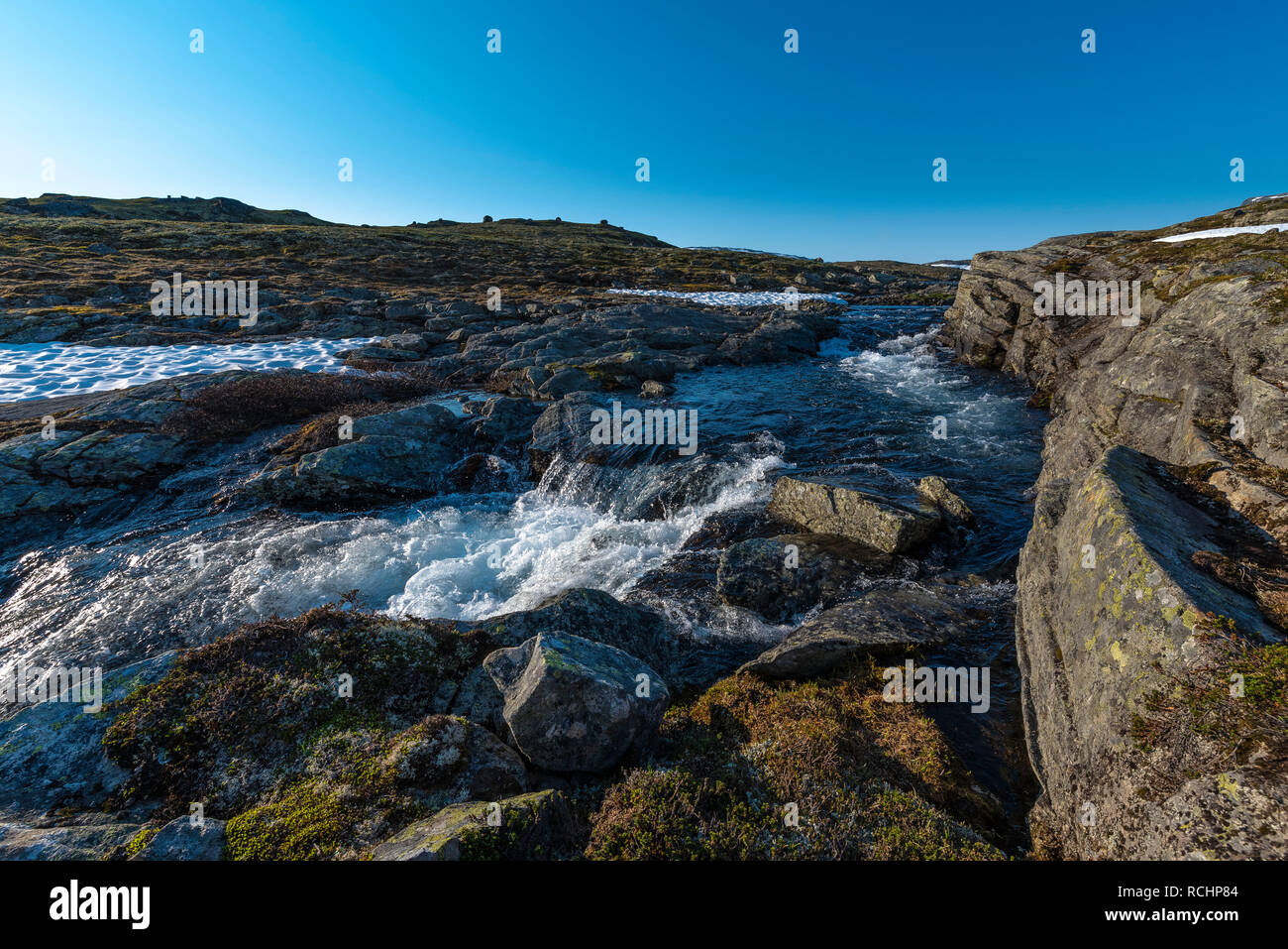 Stürmischen Strom in einem Tal mit Resten der Schnee durch die Strahlen der Morgensonne beleuchteten abgedeckt. Norwegen Aurlandsfjellet. Stockfoto