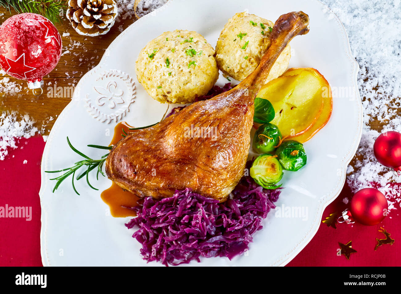 Gebratene Weihnachtsgans mit frischem Gemüse und Semmelknödel auf einer festlichen roten Tisch mit Weihnachten Dekorationen und vereinzelt Schnee von oben betrachtet serviert. Stockfoto
