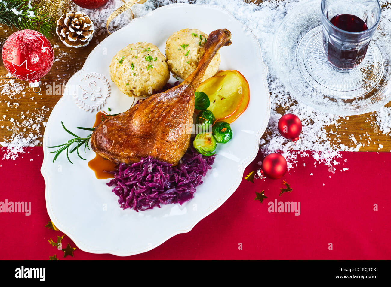Restaurant, das aus gerösteten Gans für Heiligabend mit Knödeln und frisches Gemüse auf einer festlichen roten Tisch mit Dekorationen, Rotwein und Scatte Stockfoto