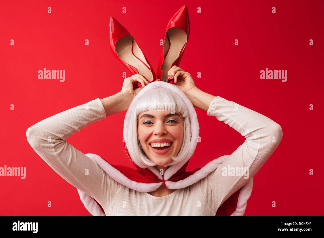 Schön lustig junge Mädchen mit roten Weihnachten kostüm stehen über den roten Hintergrund isoliert, mit High Heel Schuhe als bunny Ohren Stockfoto