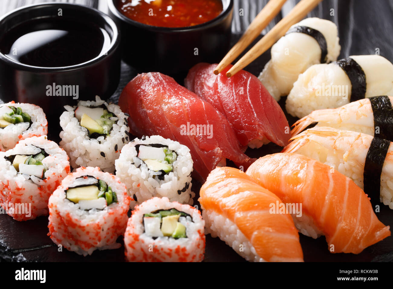 Einstellen der japanischen Rollen uramak und Nigiri serviert mit zwei Saucen close-up auf einer Schiefertafel Platte. Horizontale Stockfoto