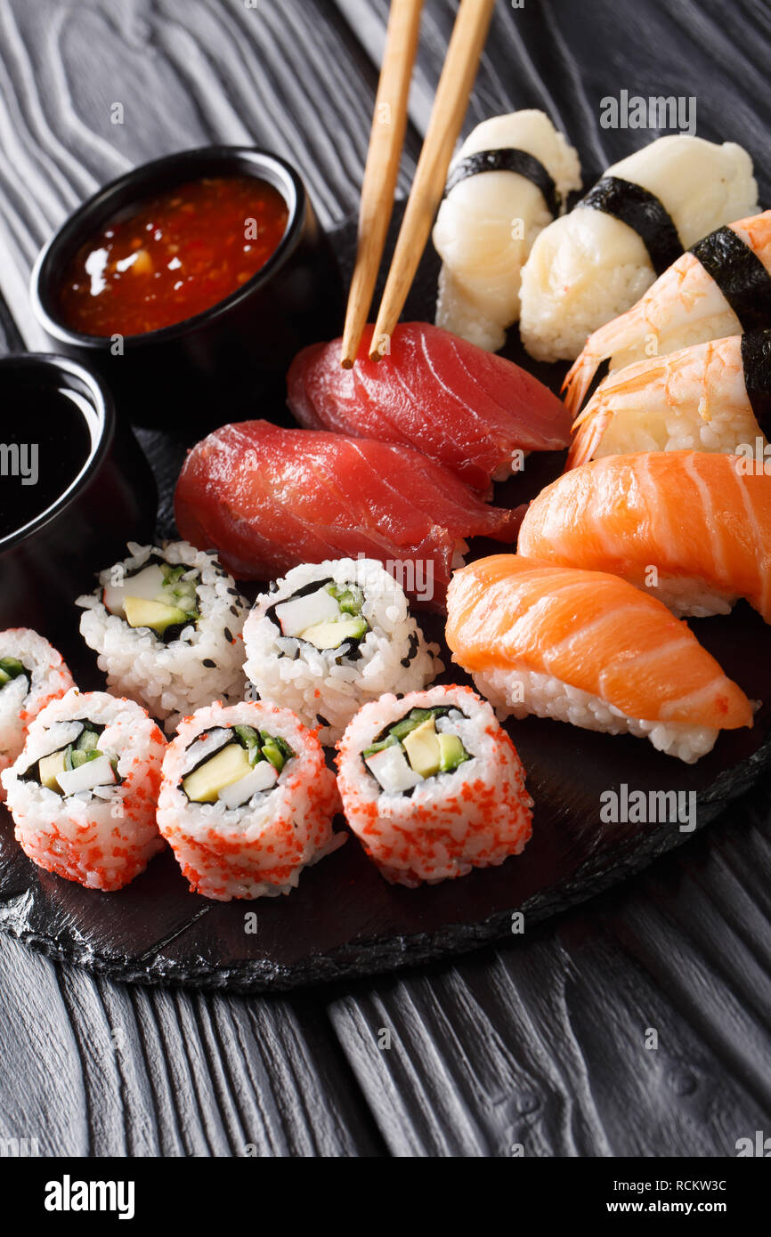 Japanisches Sushi essen. Maki ands Brötchen mit Thunfisch, Lachs, Garnelen, Krabben und Avocado mit zwei Saucen close-up auf einer Schiefertafel Platte. Vertikale Stockfoto