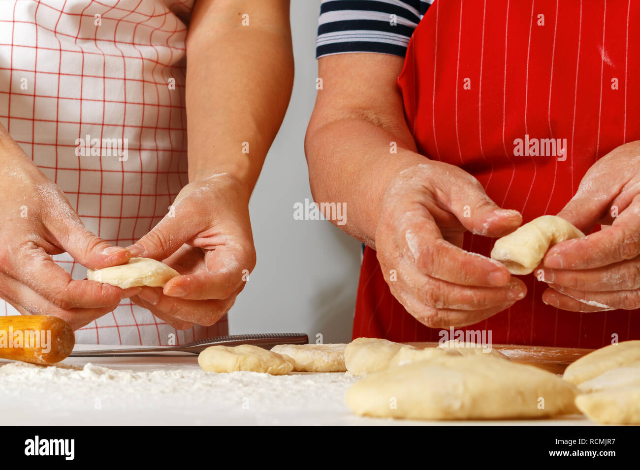 Close-up. Eine ältere Frau in einem roten Küche Schürze macht Kuchen mit einer erwachsenen Tochter Stockfoto
