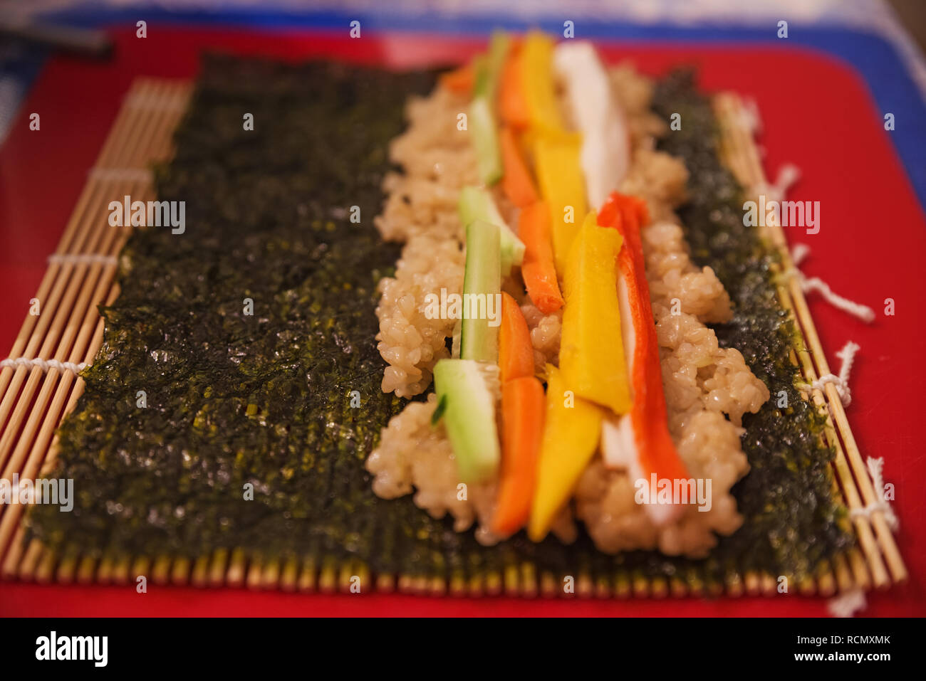 Eine selbstgemachte Sushi Roll mit Knöpfen aus Hornimitat crab mango Karotte Gurken Reis und Nori bereit zu rollen Stockfoto