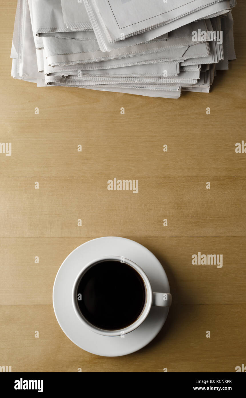 Overhead shot einer Tasse und Untertasse schwarzen Kaffee auf einem hellen Holz Laminat Tisch mit einem Stapel Zeitungen platziert. Stockfoto