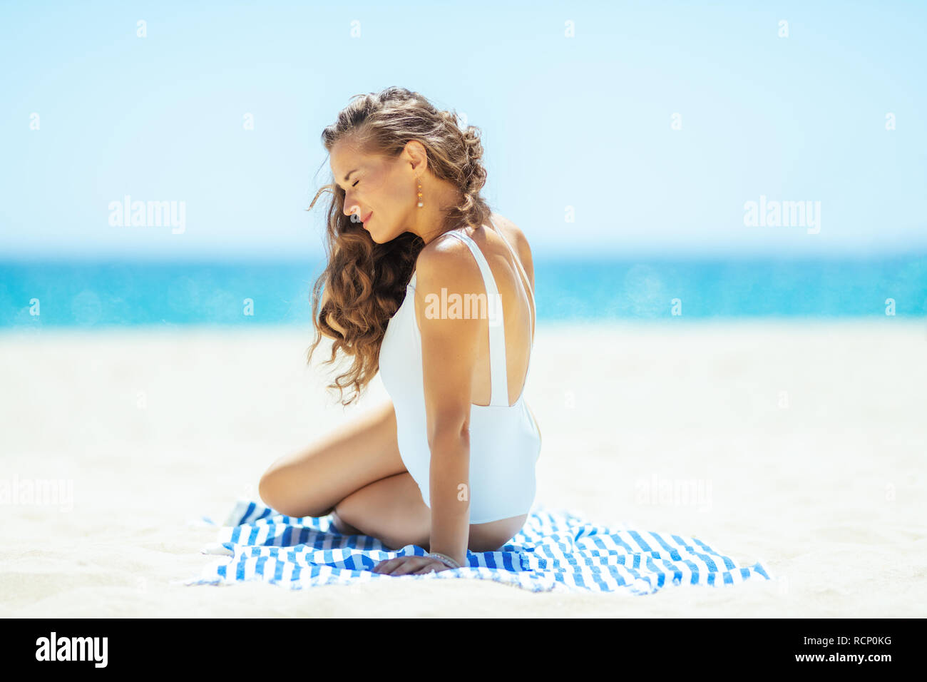 Entspannt junge Frau im weißen Badeanzug auf der Ocean Shore Standortwahl auf ein gestreiftes Handtuch. Ruhige Ferienhäuser Himmel. erste Vitamin D nach langen Wintermonaten. Stockfoto Entspannt junge Frau im weißen Badeanzug auf der Ocean Shore Standortwahl auf ein gestreiftes Handtuch. Ruhige Ferienhäuser Himmel. erste Vitamin D nach langen Wintermonaten. Stockfoto