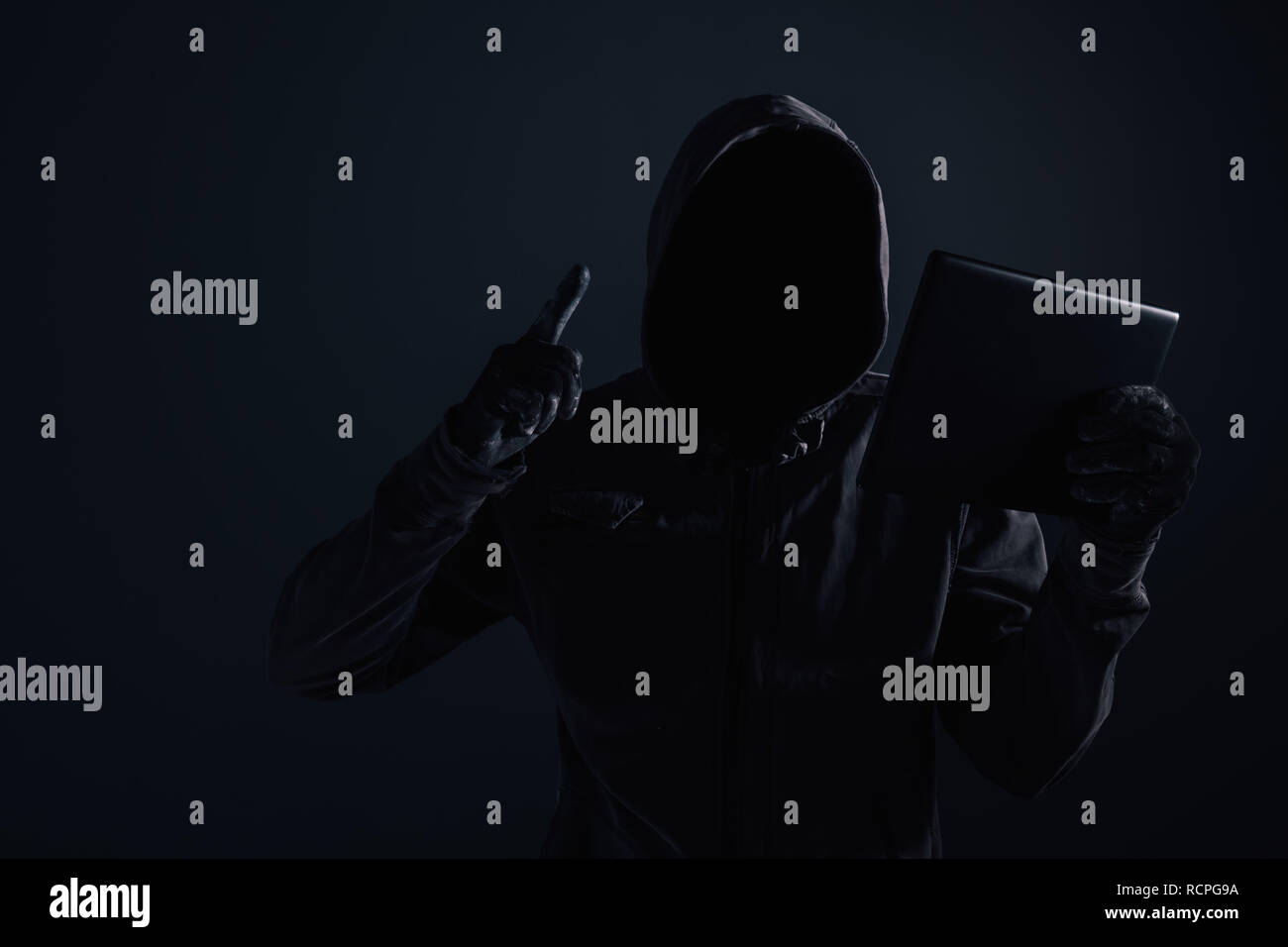 Hooded computer Hacker mit Verwendung der digitalen tablet Cyberkriminalität und Cybersicherheit Konzept verdeckt Gesicht, Low Key mit selektiven Fokus Stockfoto