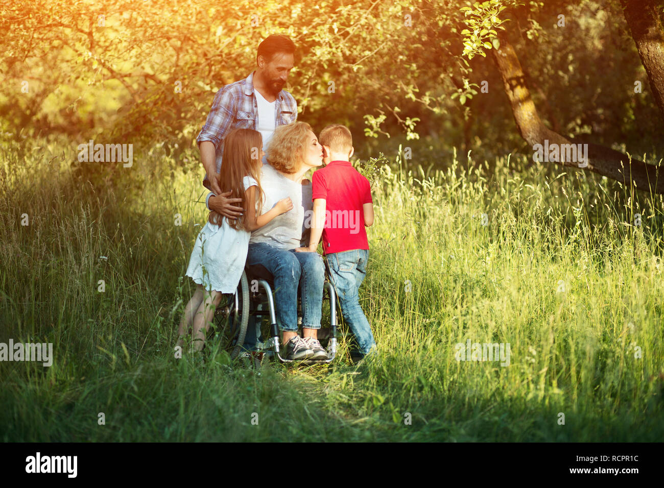 Frau im Rollstuhl küsst ihr Sohn unter Familienmitgliedern Stockfoto