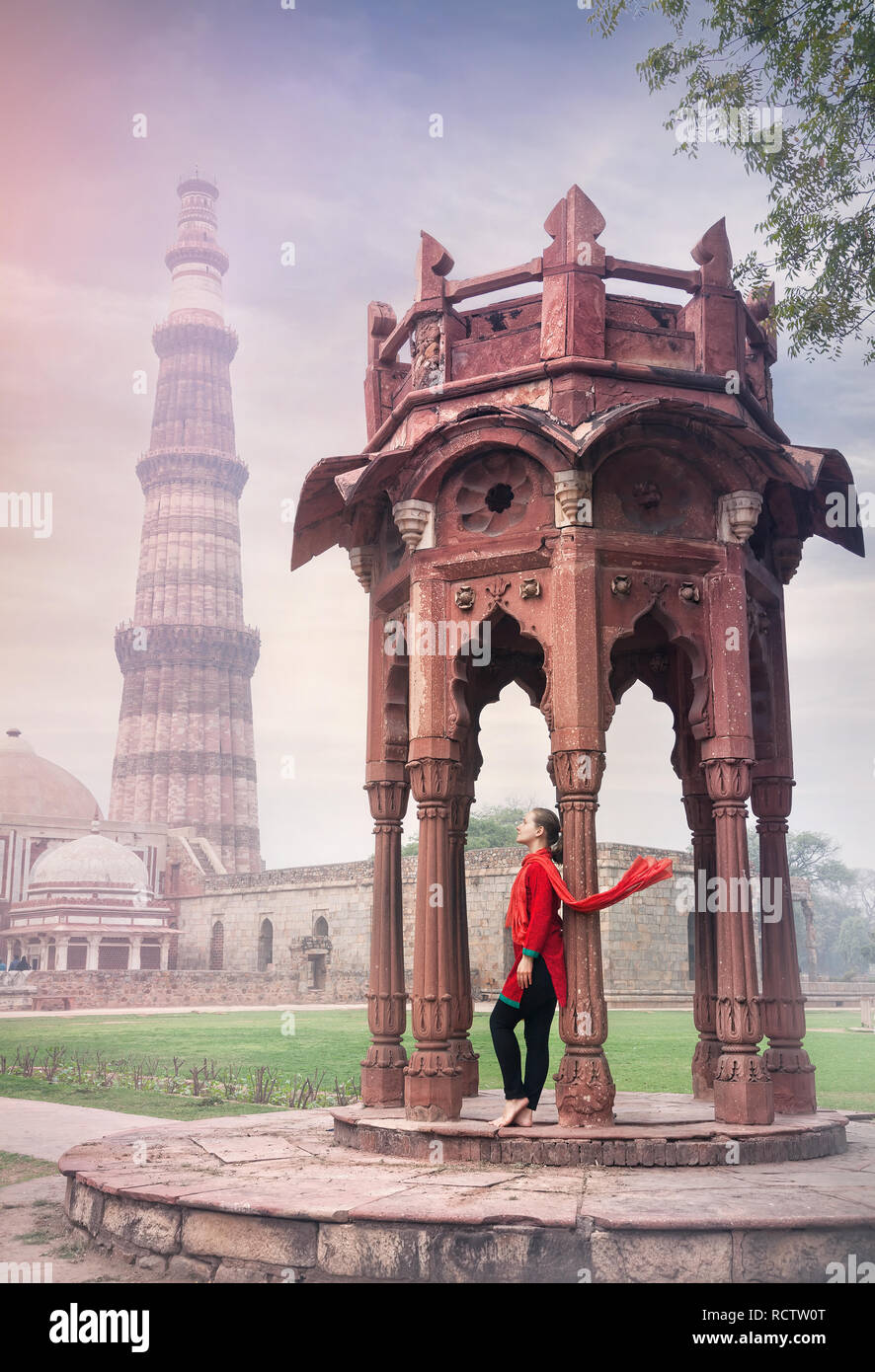 Frau in rot Kostüm mit Schal in der Nähe von Alte Architektur von Qutub Minar Turm in Old Delhi, Indien Stockfoto