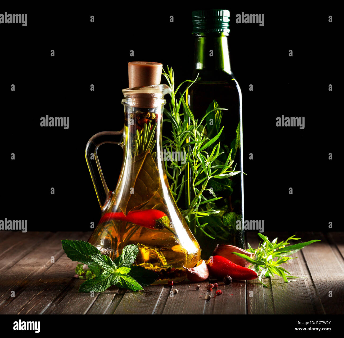 Flaschen mit Ölen, Kräutern und Gewürzen an den hölzernen Tisch auf schwarzem Hintergrund Stockfoto