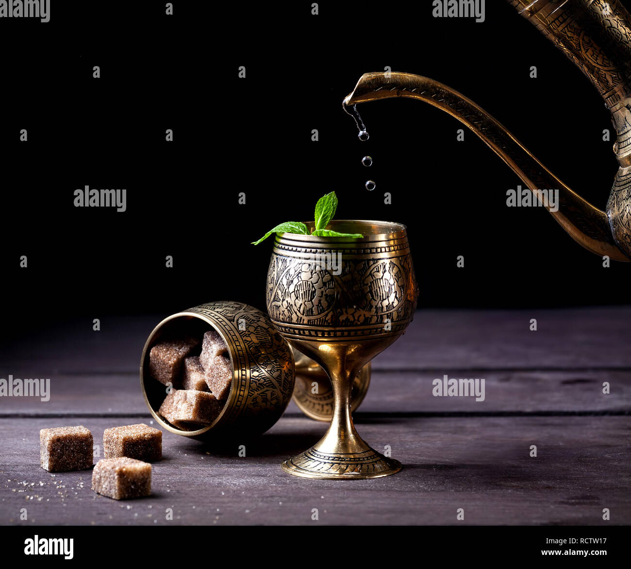 Marokkanischen Tee mit Minze gießen aus der orientalischen Cooper Pot in Schale auf rustikalen Holzmöbeln Hintergrund Stockfoto
