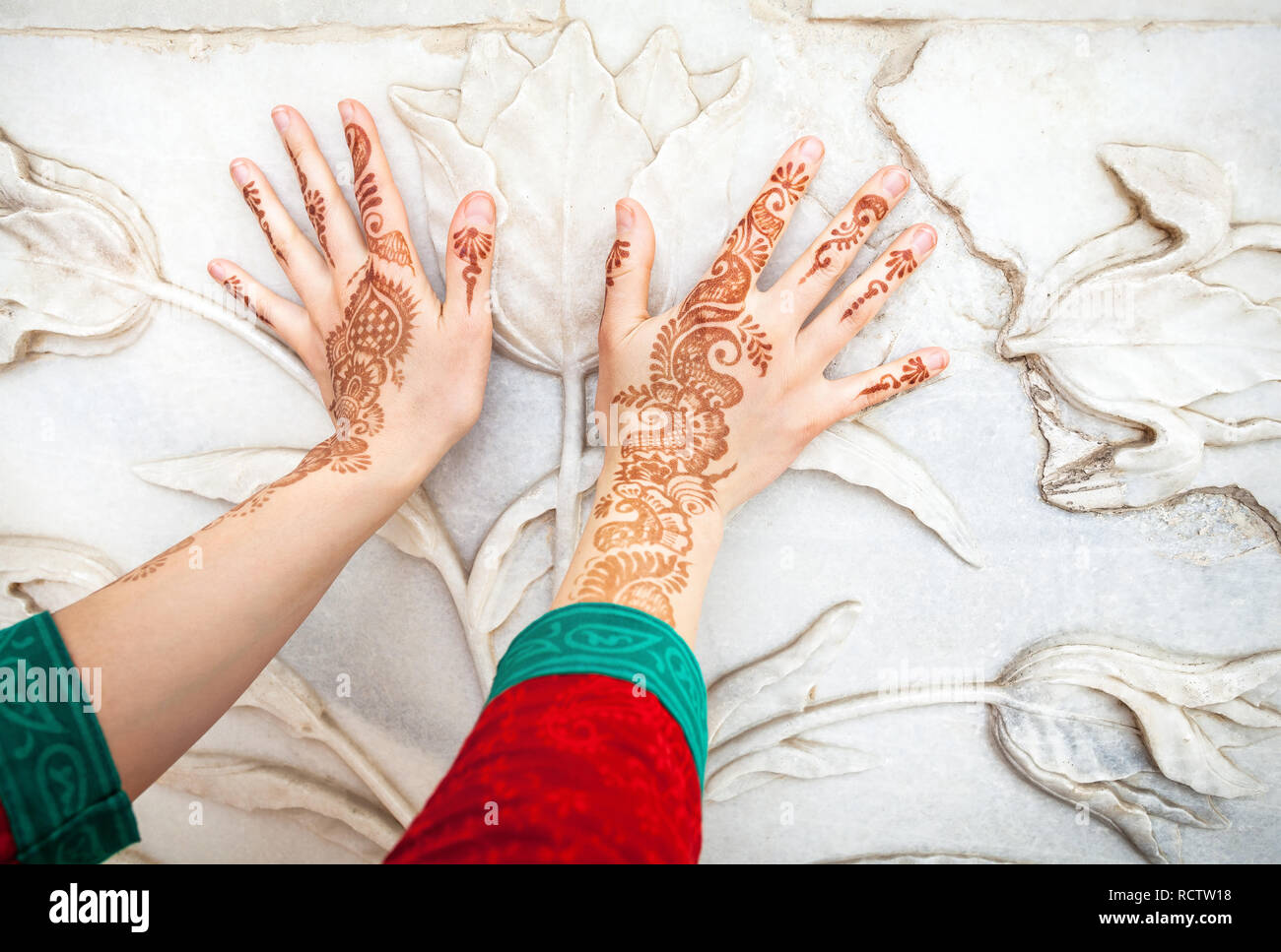 Frau in rot Indischen Kostüm berühren weißer Marmor Wand mit floralen Muster von Hände in Hennamalerei im Taj Mahal in Agra, Uttar Pradesh, Indien Stockfoto