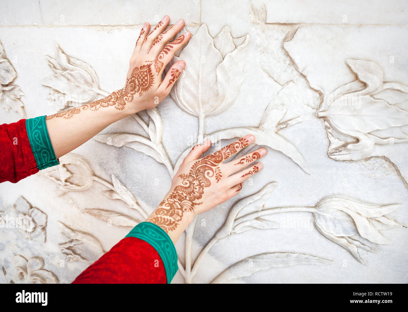 Frau in rot Indischen Kostüm berühren weißer Marmor Wand mit floralen Muster von Hände in Hennamalerei im Taj Mahal in Agra, Uttar Pradesh, Indien Stockfoto