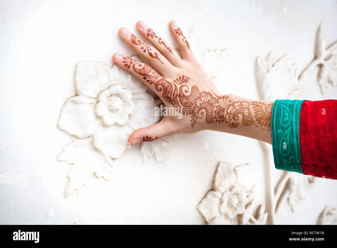 Frau in rot Indischen Kostüm berühren weißer Marmor Wand mit floralen Muster von Hand in Hennamalerei im Taj Mahal in Agra, Uttar Pradesh, Indien Stockfoto