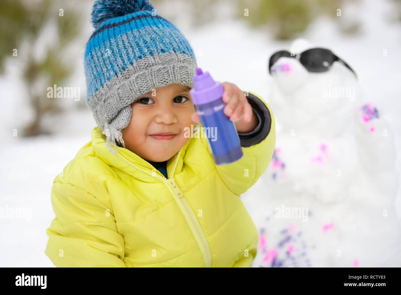 Cute Hispanic junge im Winter Kleidung spielen mit Farben und einen Schneemann in einem schneebedeckten Berg während der Wintersaison. Stockfoto