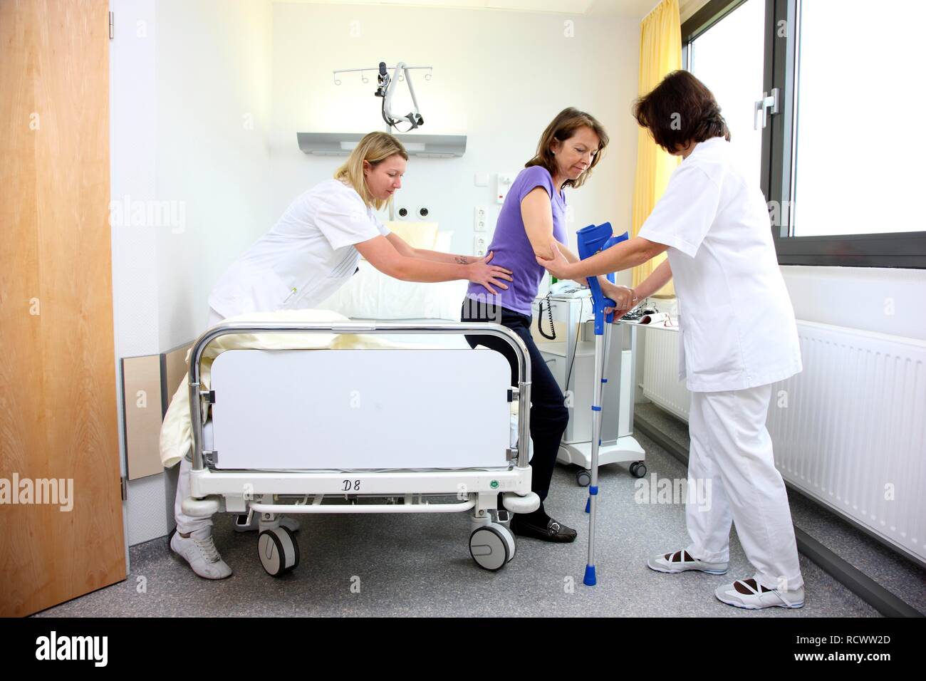 Krankenschwestern die Unterstützung eines Patienten versuchen, mit Gehhilfen laufen, die Mobilisierung nach der Operation im Krankenhaus Stockfoto