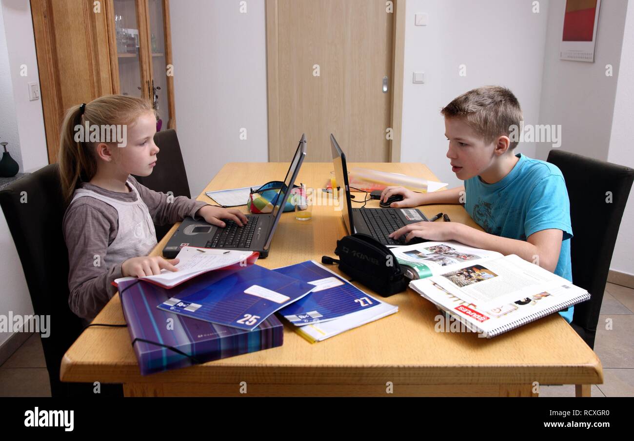 Geschwister, Bruder und Schwester, die beide an einem Notebook arbeitet, um gemeinsam Hausaufgaben zu machen im Wohnzimmer Stockfoto
